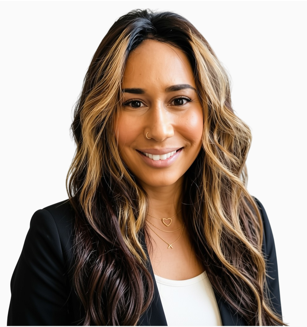 A woman with wavy, blonde and dark brown hair, smiling, wearing a black blazer and layered necklaces, standing against a white background.