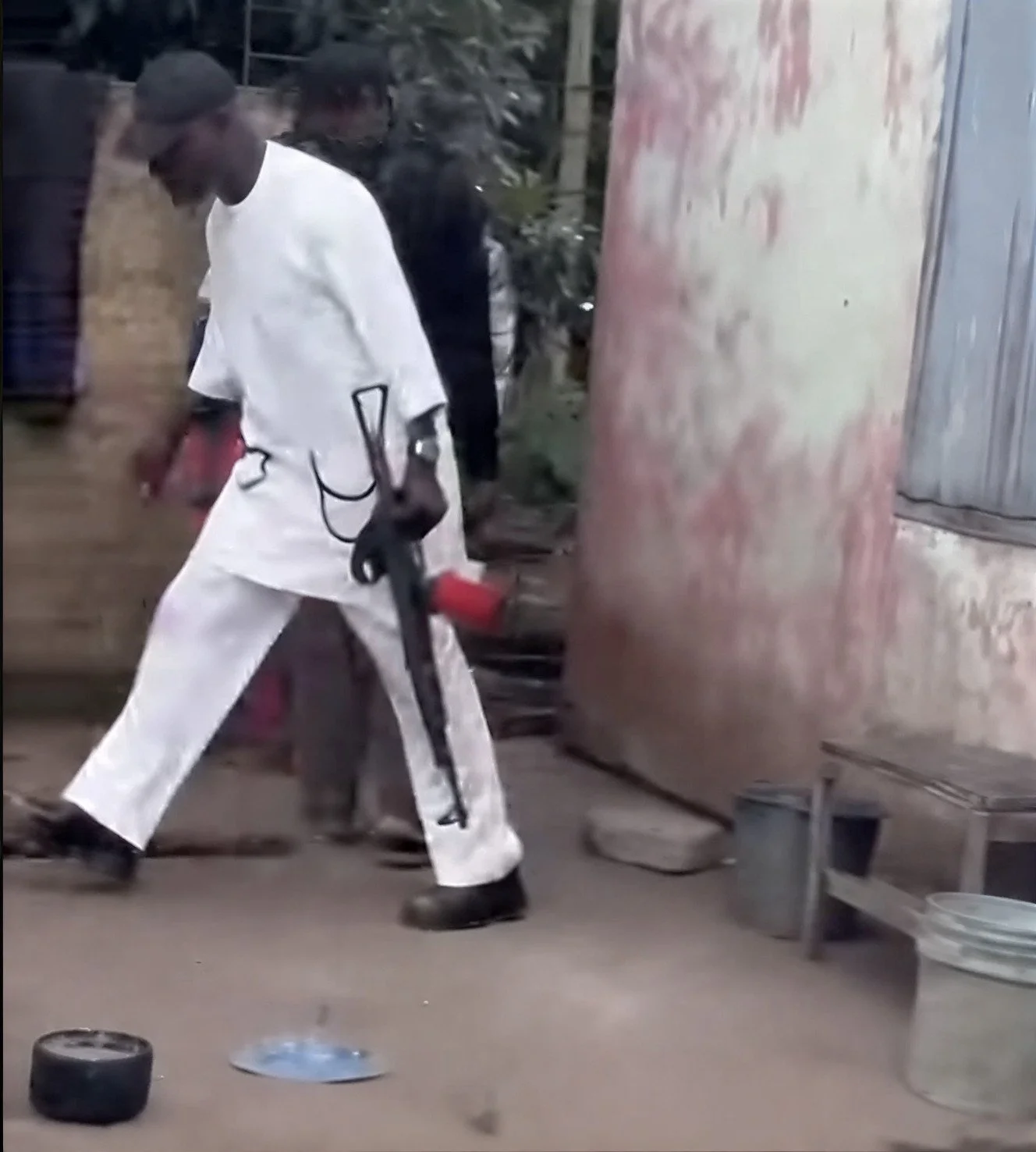 A tall Nigerian in a white pajama-kurta carrying a big semi-automated rifle.