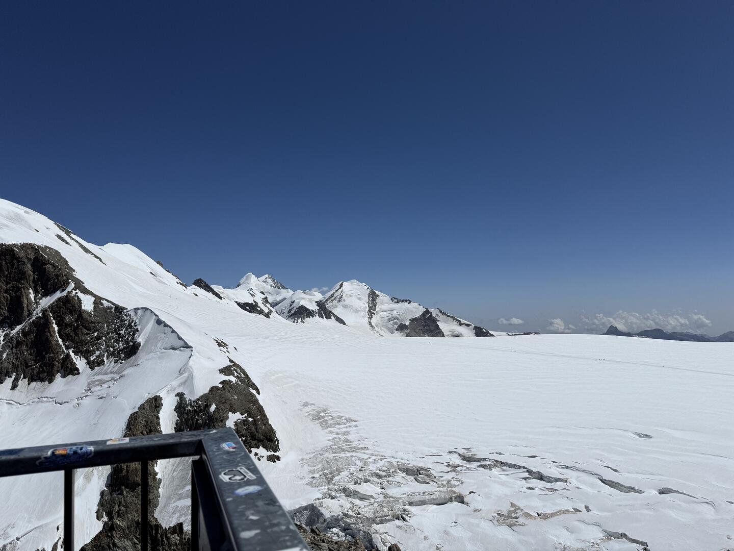 This image shows a snow-covered area of Zermatt, Switzerland; one can also see a clear blue sky, rocks, and a corner of some balcony.