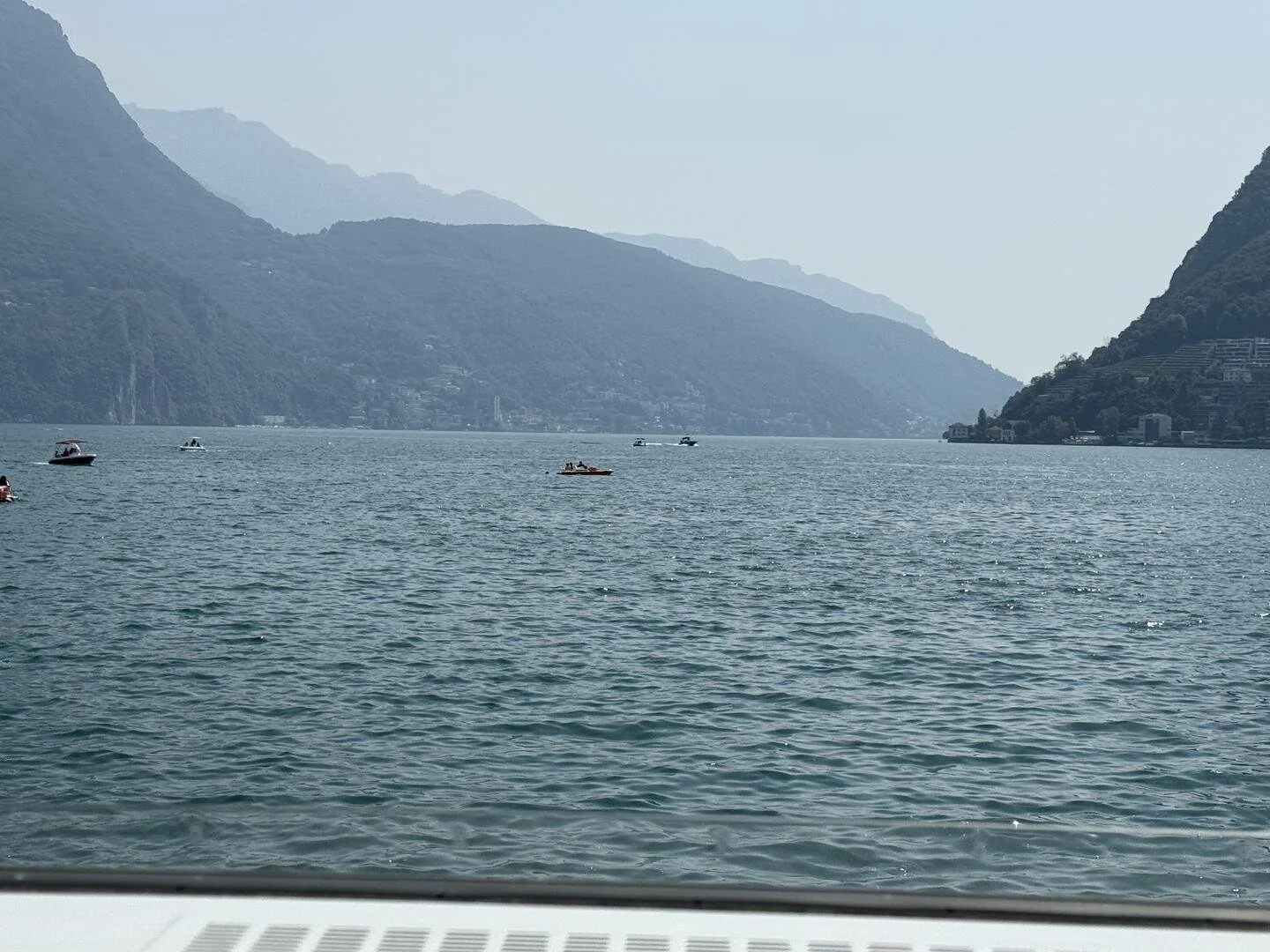 This is broad view of Lake Brienz, Switzerland, taken by Dr. Namita Sethi.  The photograph shows blurry bluish hills in the background; in the foreground one sees bluish waters, and around 5 small boats in the distance.  One can also see blue sky.