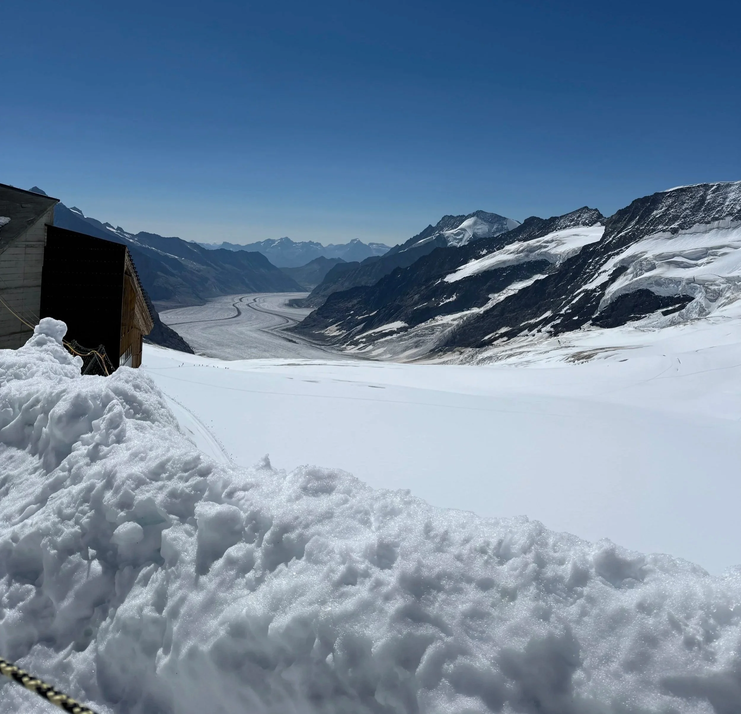 This is a photograph of Jungfraujoch, Switzerland, taken by Dr. Namita Sethi of India in August 2025.  This photograph shows snow, a blue sky, and rocky hills of the area.