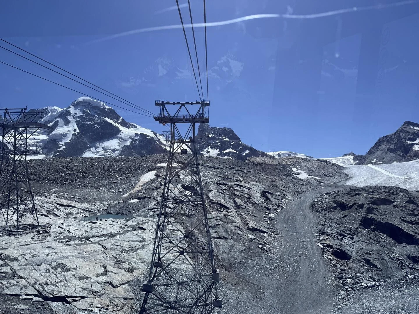 This image shows a part of the ropeway infrastructure in Zermatt, Switzerland, underneath a blue sky.  One can also see a rocky area and snow-covered hills.