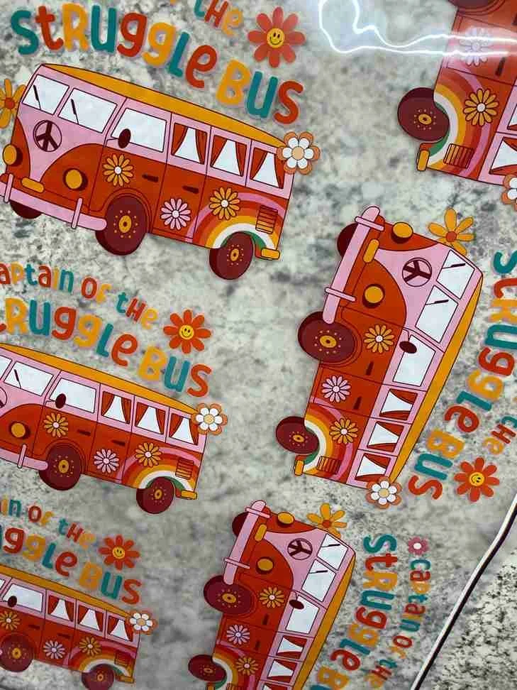 Pattern with cartoon illustrations of a San Francisco-style trolley bus decorated with flowers, and the text 'The Struggle Bus' repeated in colorful letters.