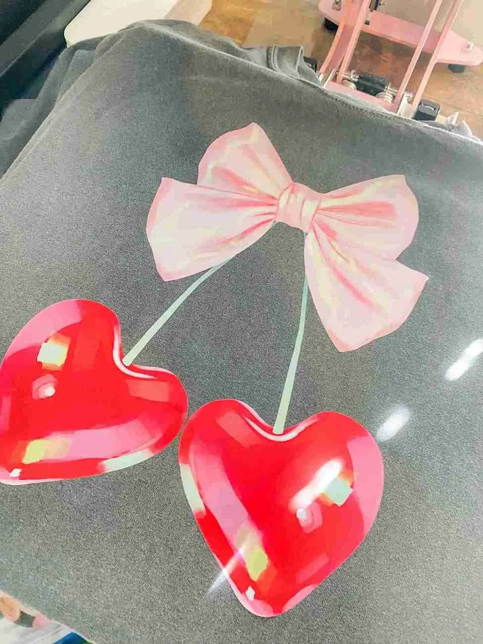 Decorative paper cutout of a pink bow and two red hearts on a gray surface.
