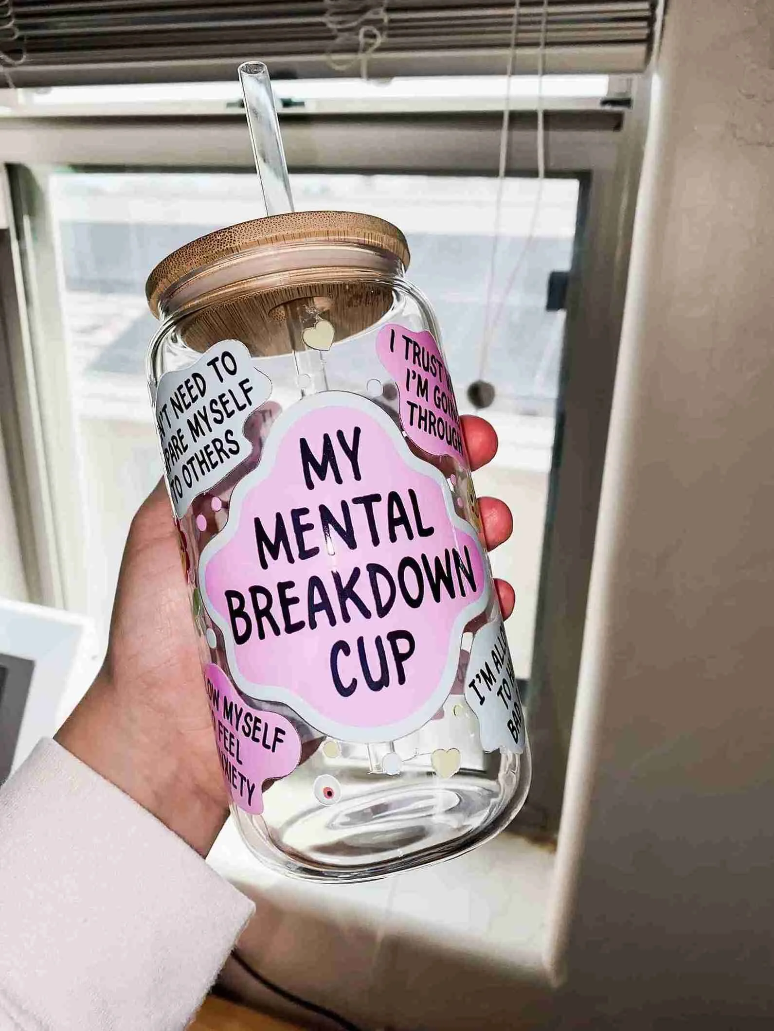 Clear water tumbler with a wooden lid and straw labeled 'My Mental Breakdown Cup' with various stickers expressing feelings of vulnerability and trust.