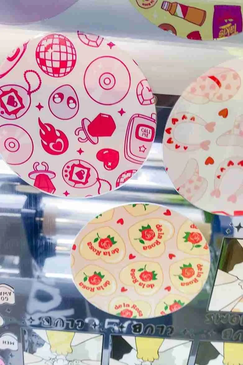 Three round stickers with different Valentine-themed designs, including pink icons, hearts, roses, and cute illustrations.