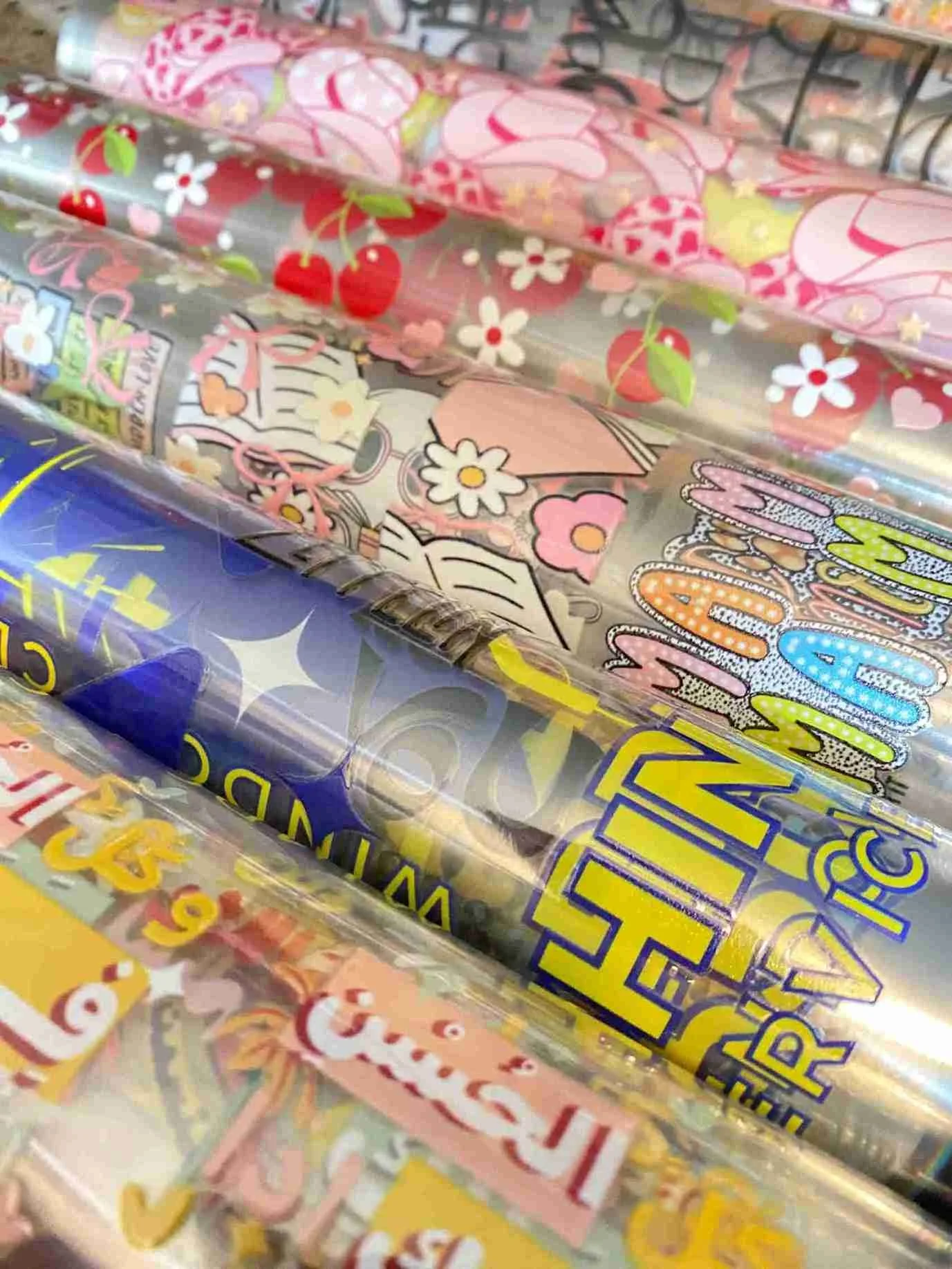 A close-up view of multiple rolls of decorative film with various colors and patterns, including flowers, cherries, and cartoon-like designs.