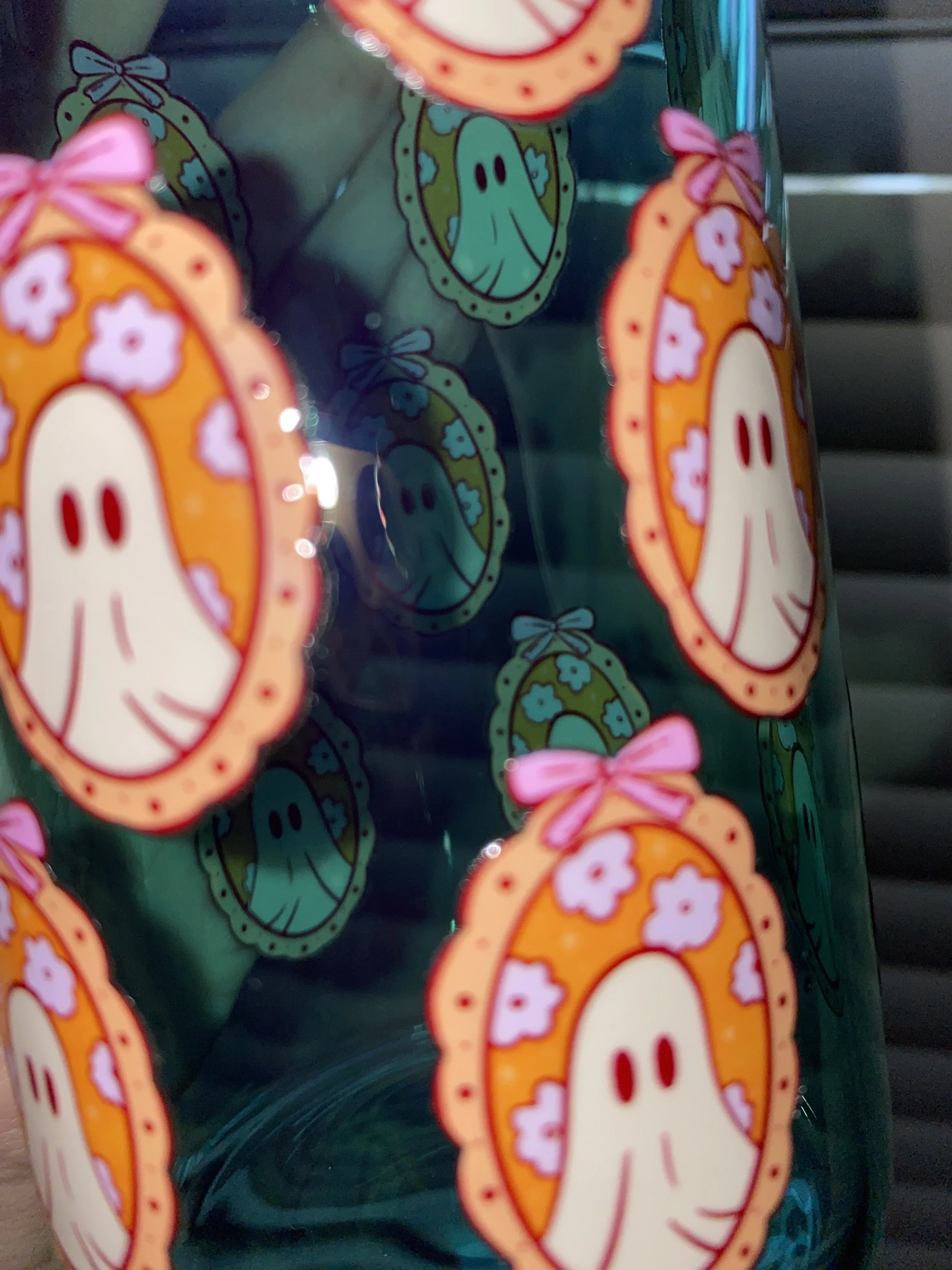 Decorative stickers of a cartoon ghost with a pink bow, surrounded by a pink floral pattern, on a green surface, viewed through a transparent plastic container.