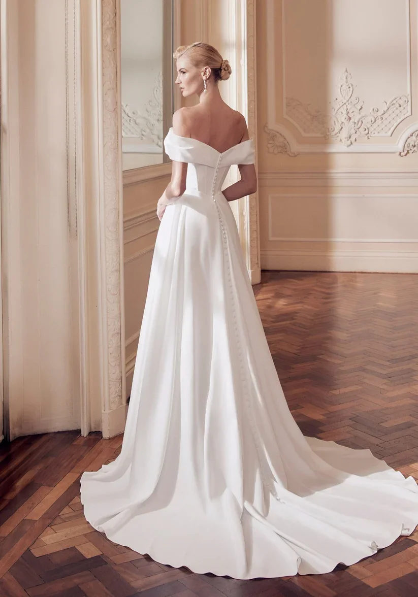 Wilma is a crepe A-line gown. Her Bardot neckline twists across the bust, and a soft, graceful skirt. Wilma captures the perfect blend of sculptural elegance and fluidity, allowing for movement that feels light and natural.