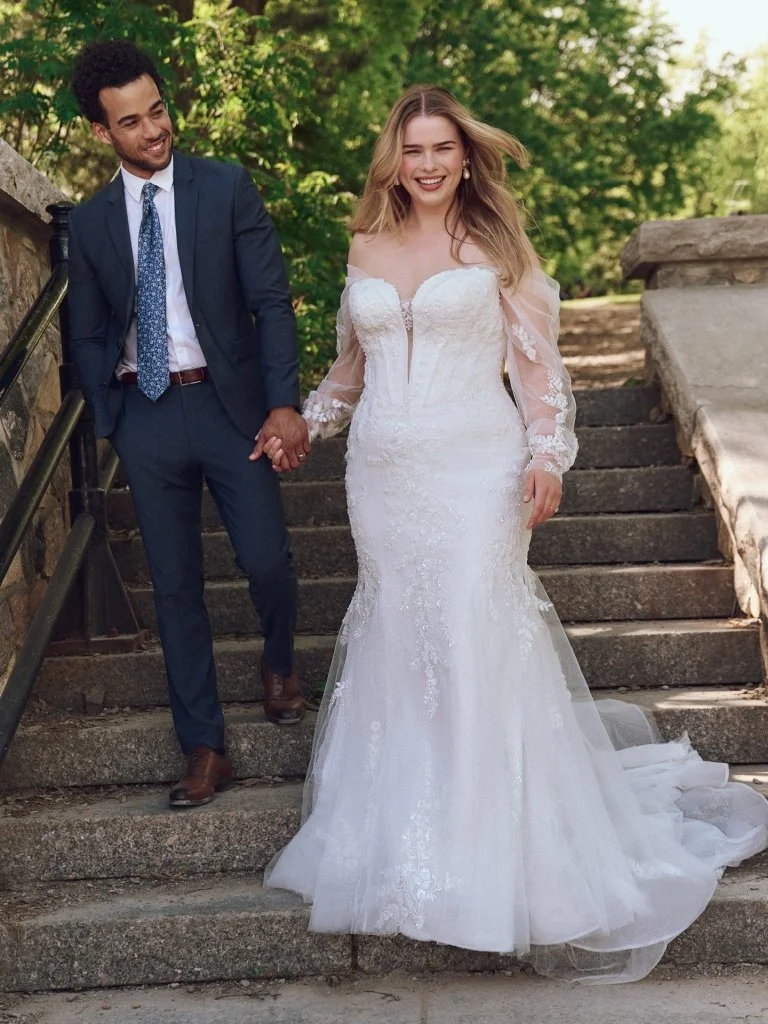 A bride and groom holding hands on outdoor stone steps, smiling with trees in the background.