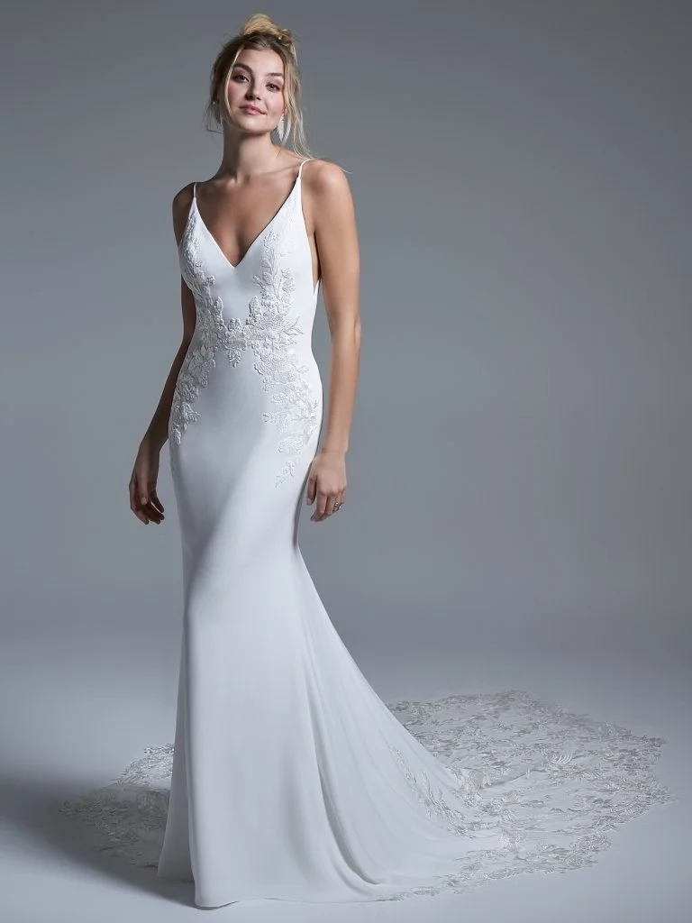 Woman in a white wedding dress with lace details, standing on a plain gray background.
