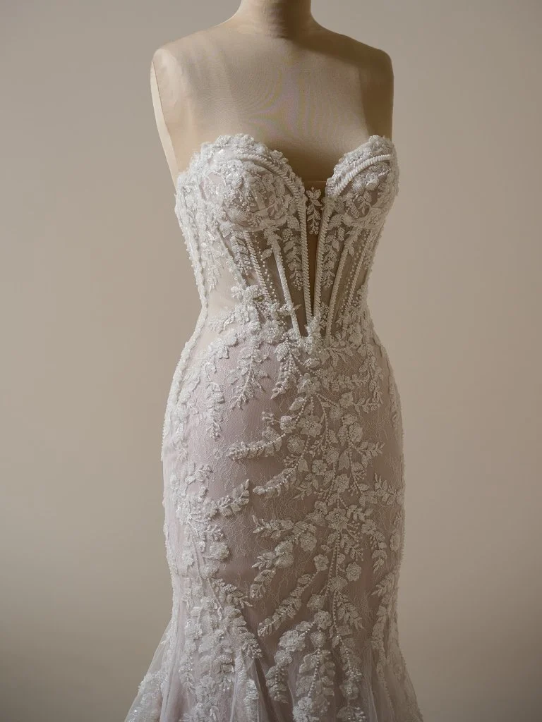 A white lace wedding dress with floral embroidery and a fitted silhouette, displayed on a mannequin.