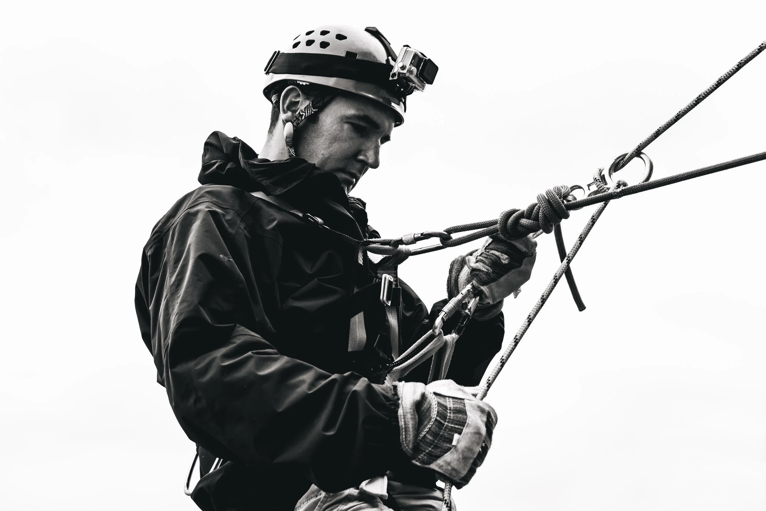 A person wearing a helmet with a camera mounted on it, engaged in rock climbing or rappelling, holding onto ropes.