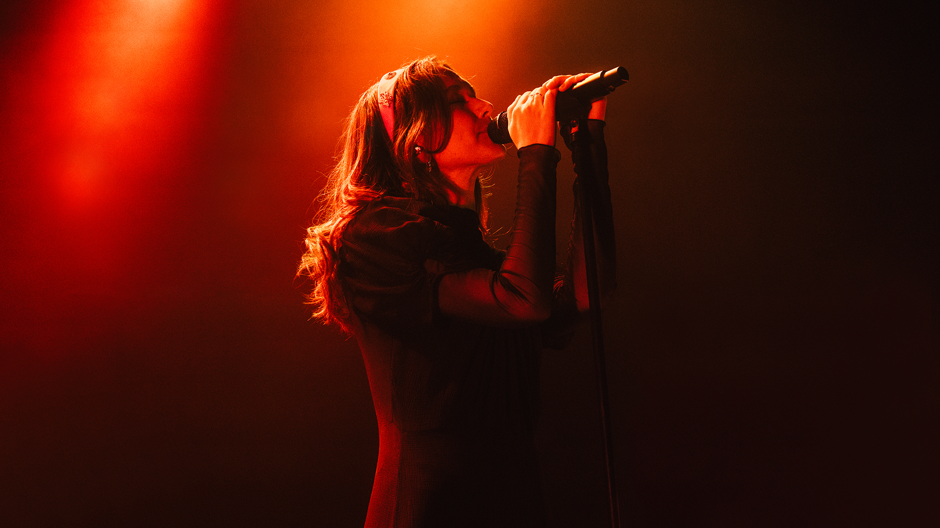 Canadian singer Ghostly Kisses singing into a microphone on stage, illuminated by red and yellow stage lights.