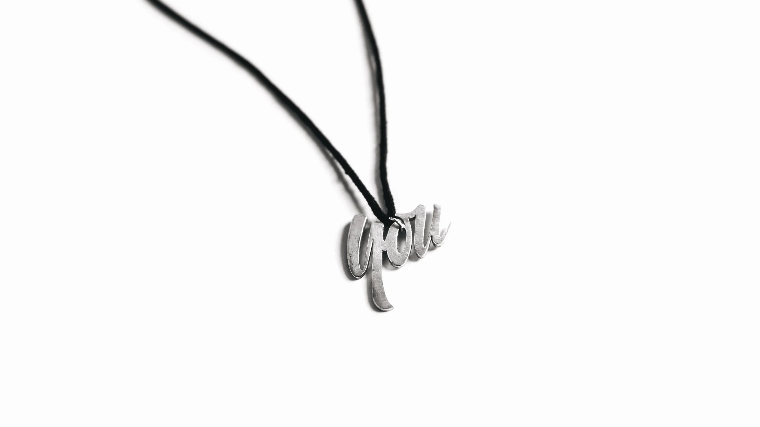 Close-up of a silver 'girl' word necklace with black cords on a white background.