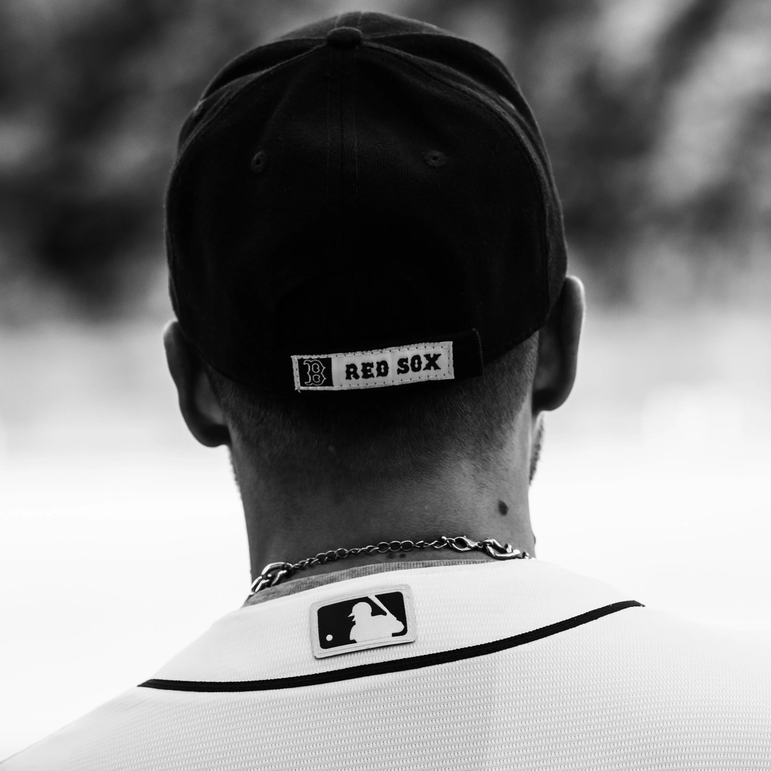 Back of a person wearing a black baseball cap and a white sports jersey with Major League Baseball logo.