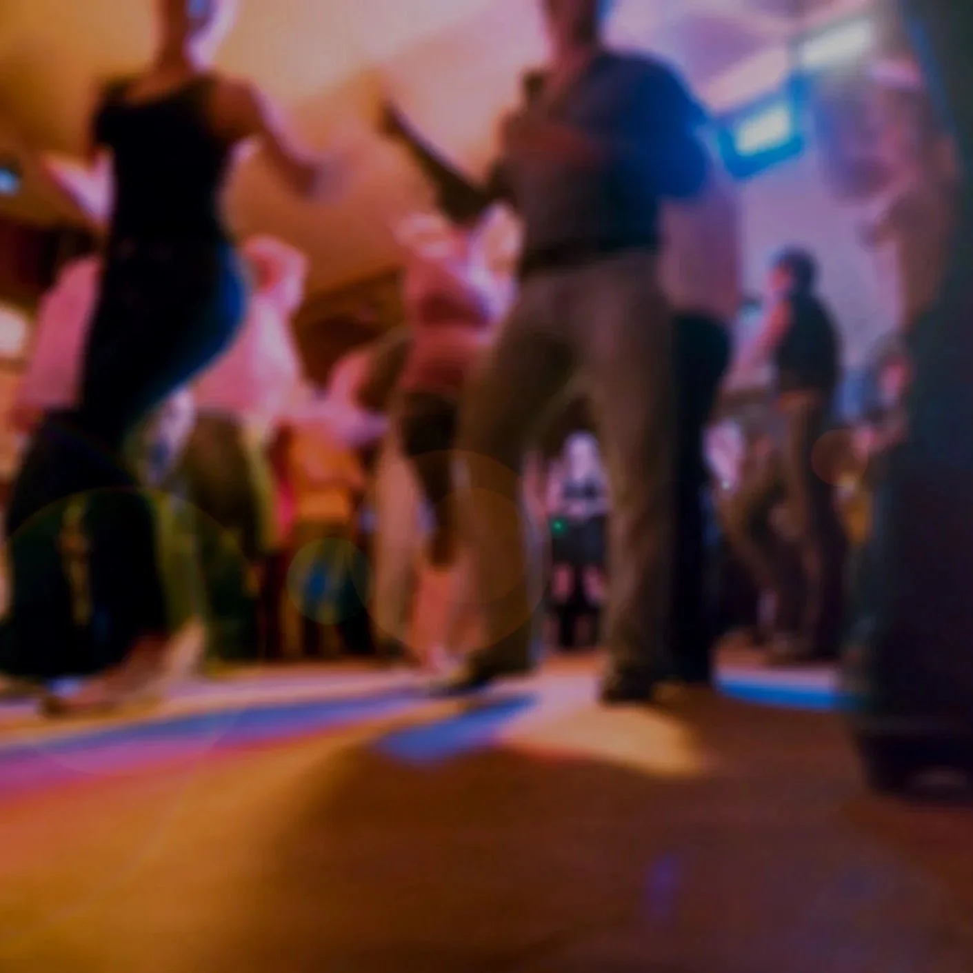 People dancing on a dance floor in a dimly lit nightclub with colorful lights.