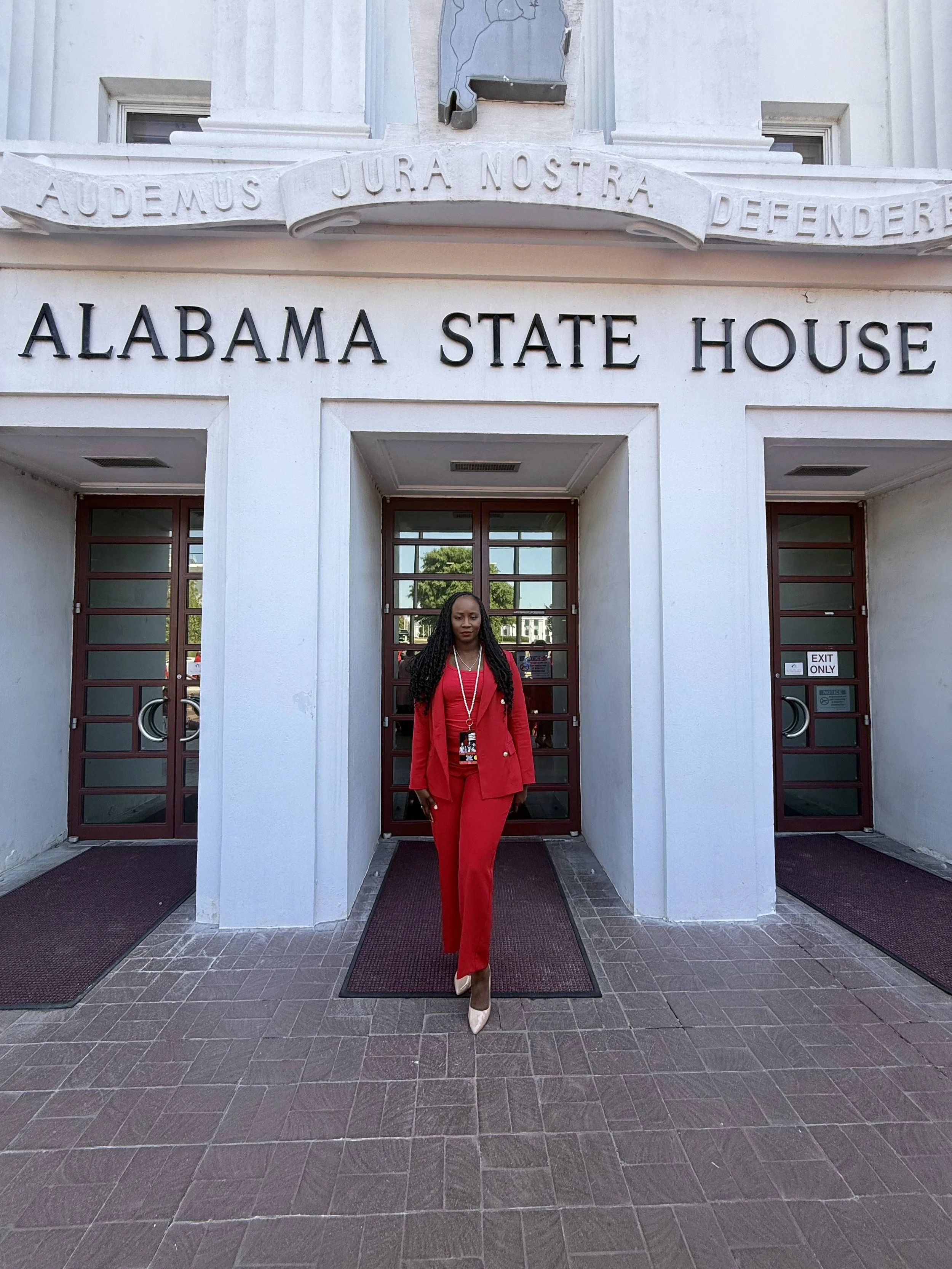 A woman dressed in red standing in front of the Alabama State House building.