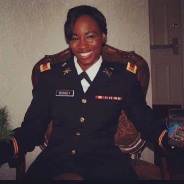 A woman in a military uniform sitting on a chair and smiling at the camera.