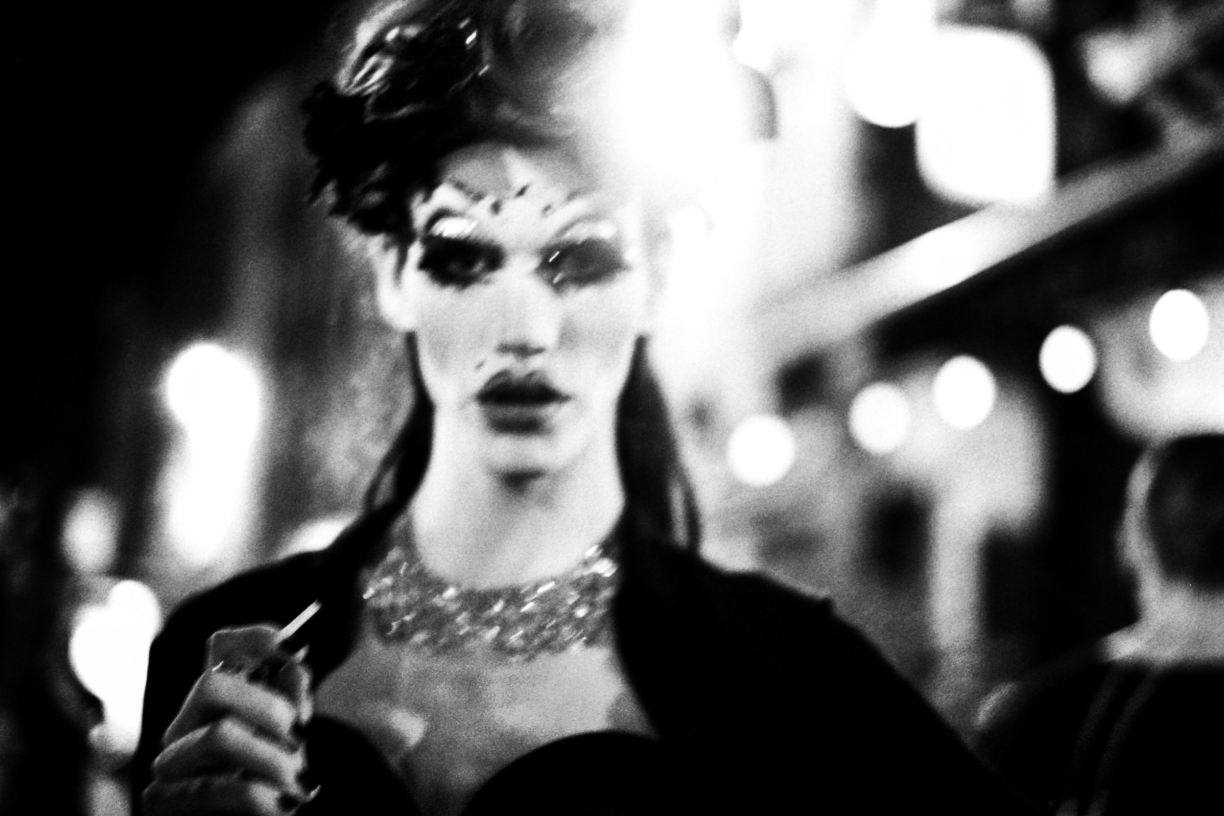 A woman with styled hair and makeup, holding a sparkler, at night with blurred lights in the background.