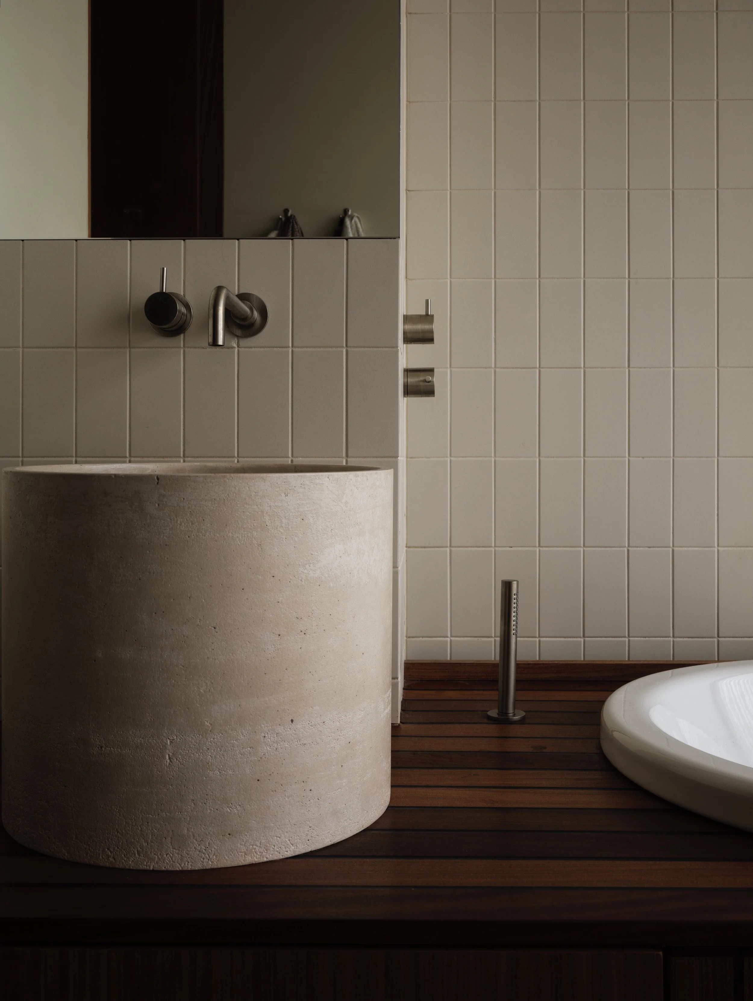 Modern bathroom with round concrete sink, wall-mounted faucet, wooden countertop, and white tiled wall.