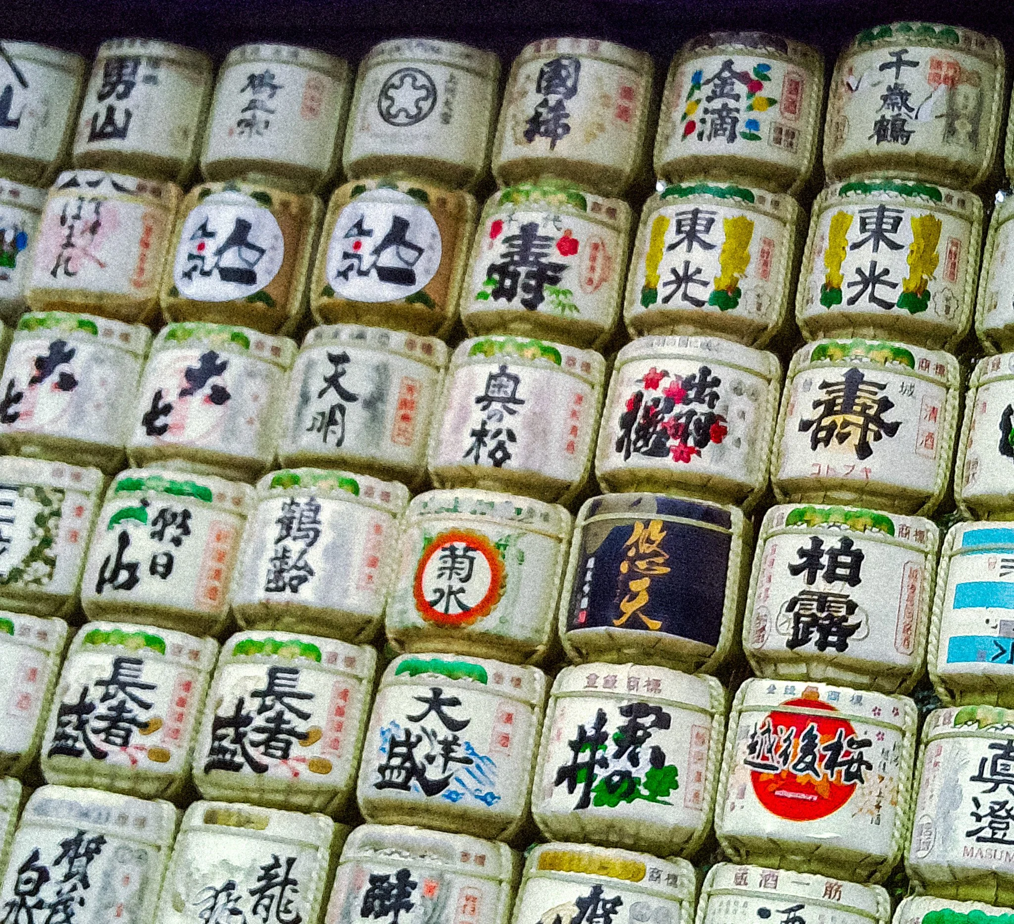 Close-up of multiple traditional Japanese sake barrels decorated with Japanese characters and colorful designs, arranged in rows.