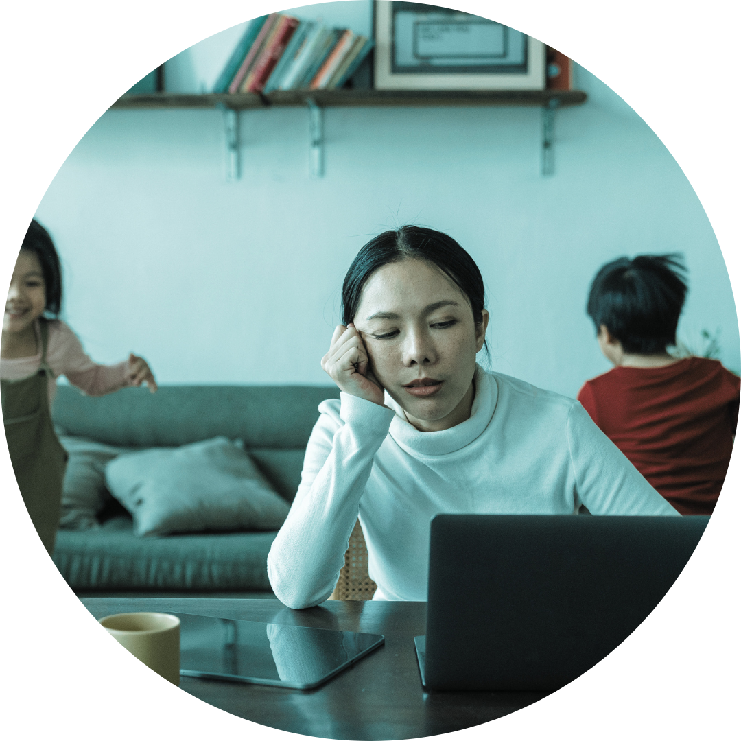 Woman-mother sitting at laptop looking tired with kids behind her