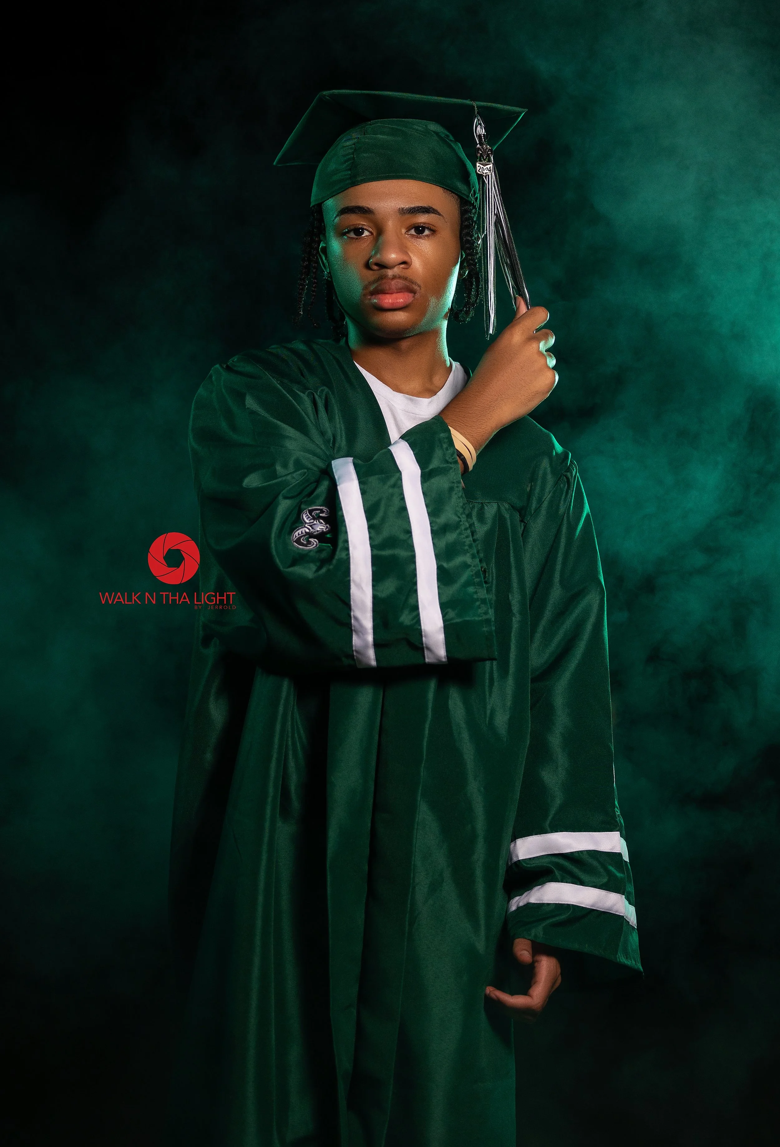Person in green graduation gown and cap holding tassel in front of foggy green background.