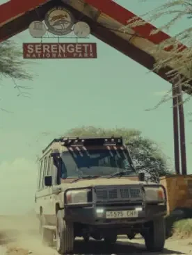Eingangstor mit 'Serengeti National Park' Schilder und ein geländewagen auf der Straße.