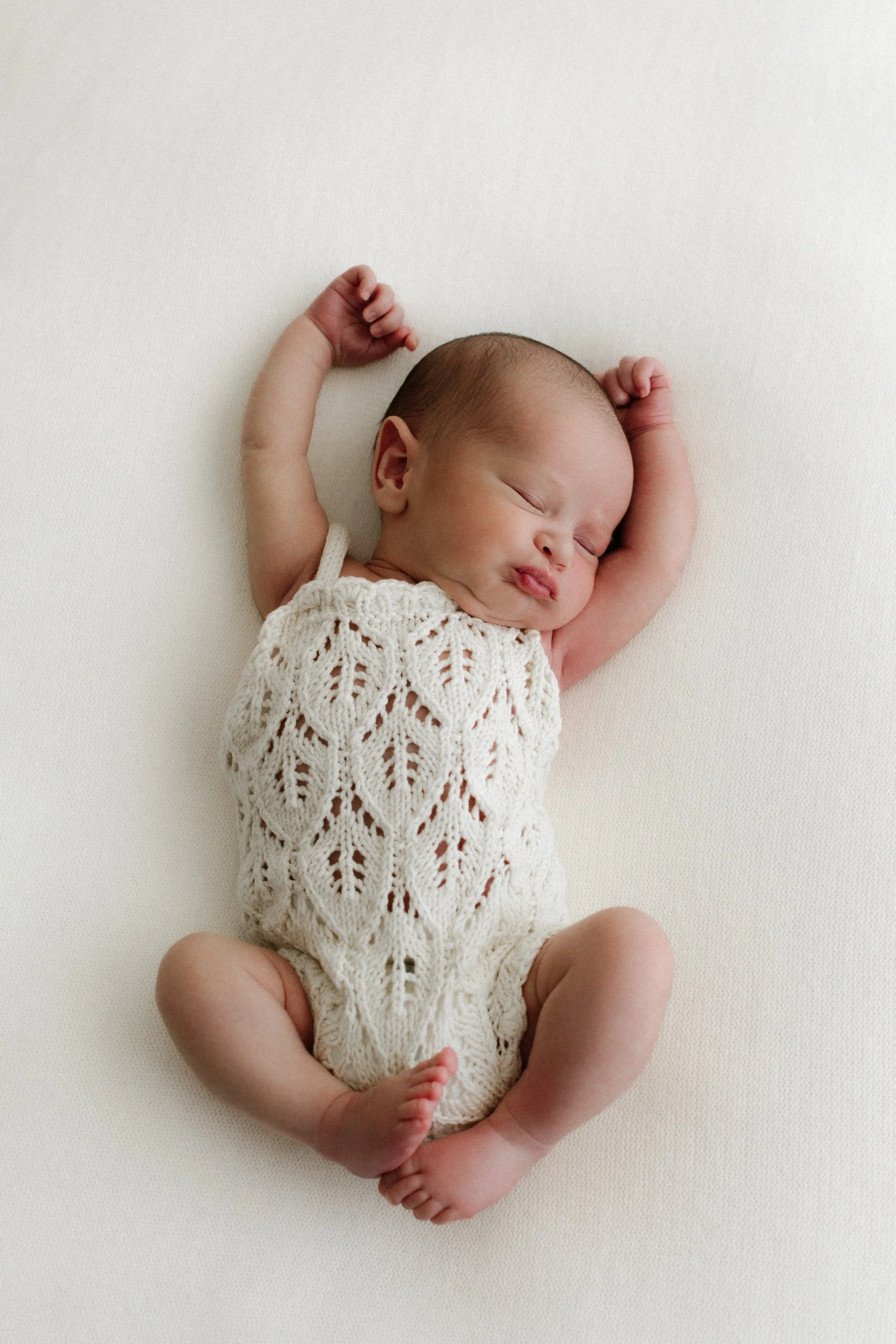 Baby newborn stretching during photoshoot in a timeless white setting