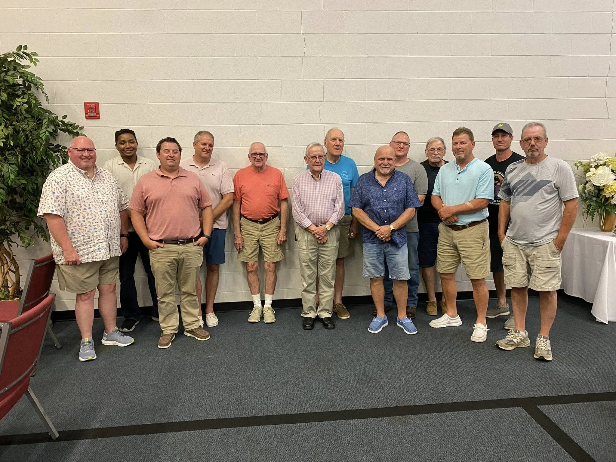 A person in a long-sleeve shirt eating a meal with a plate of food that includes bread, beans, vegetables, and possibly a cooked chicken leg, with a glass of drink on the side.