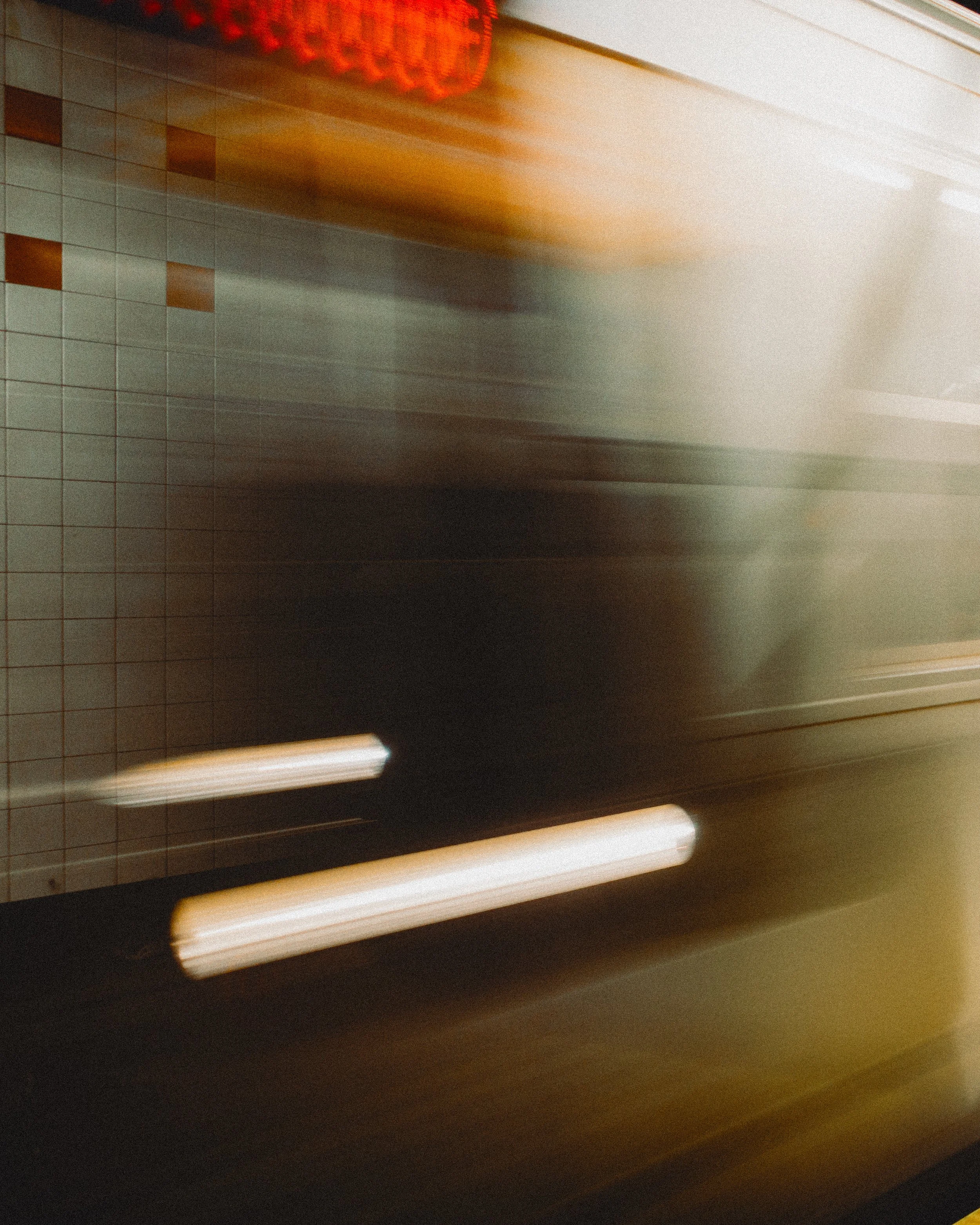 Blurry image of a tiled wall and bright horizontal lights, possibly taken in a restaurant or public space with artificial lighting.