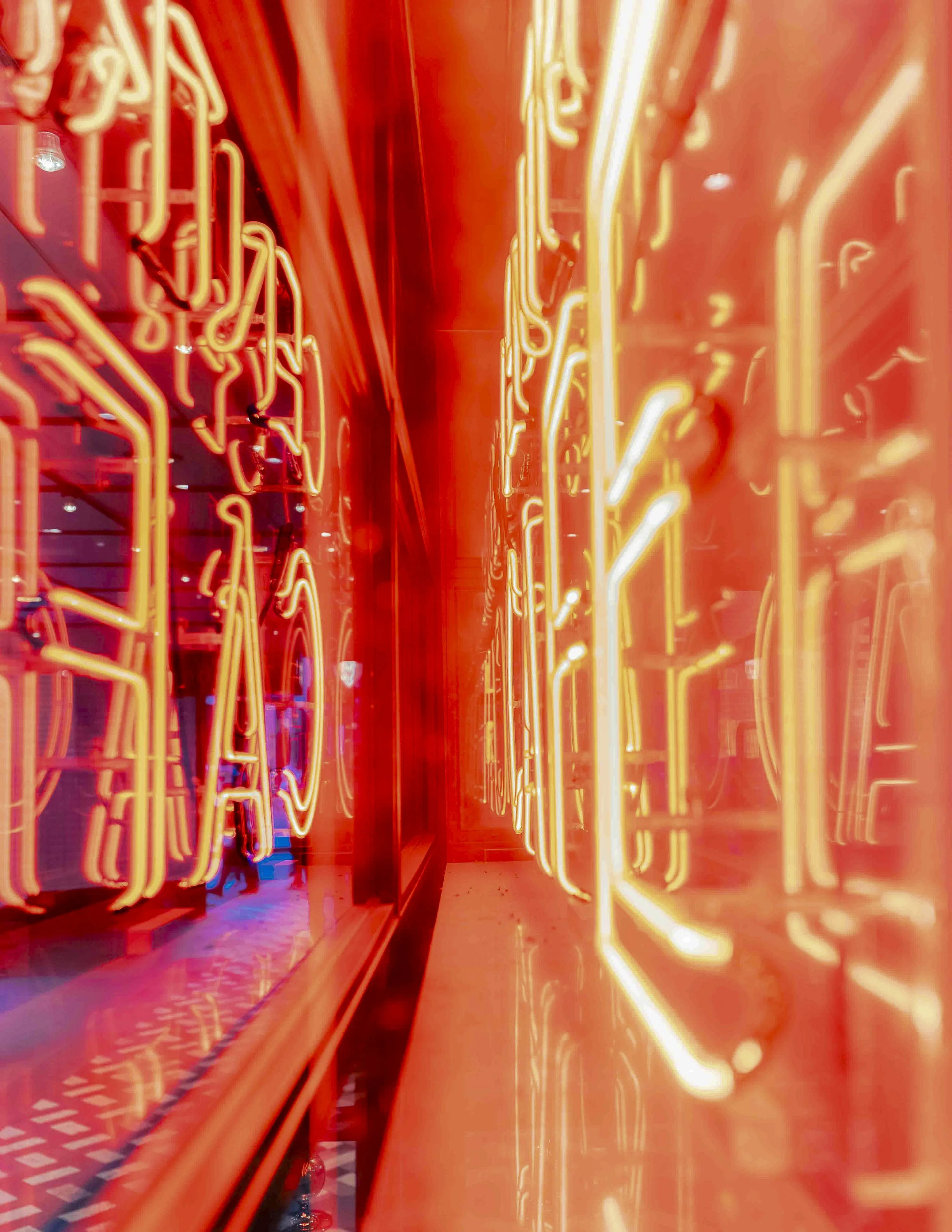 Close-up view of neon lights reflecting on a shiny surface, creating a vibrant, glowing corridor with red and orange hues.