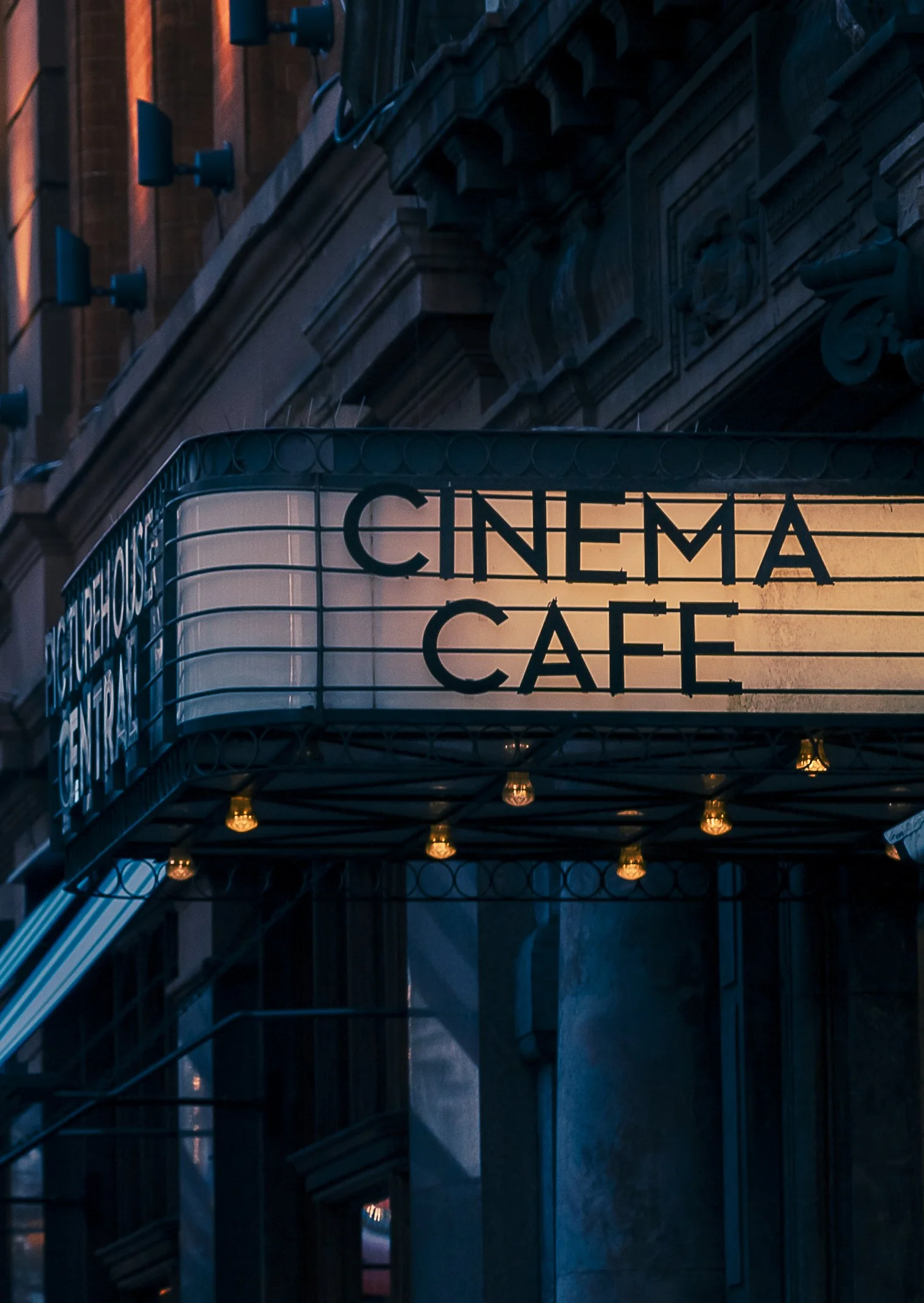 Neon sign for a cinema café on a building in an urban setting, illuminated at dusk.