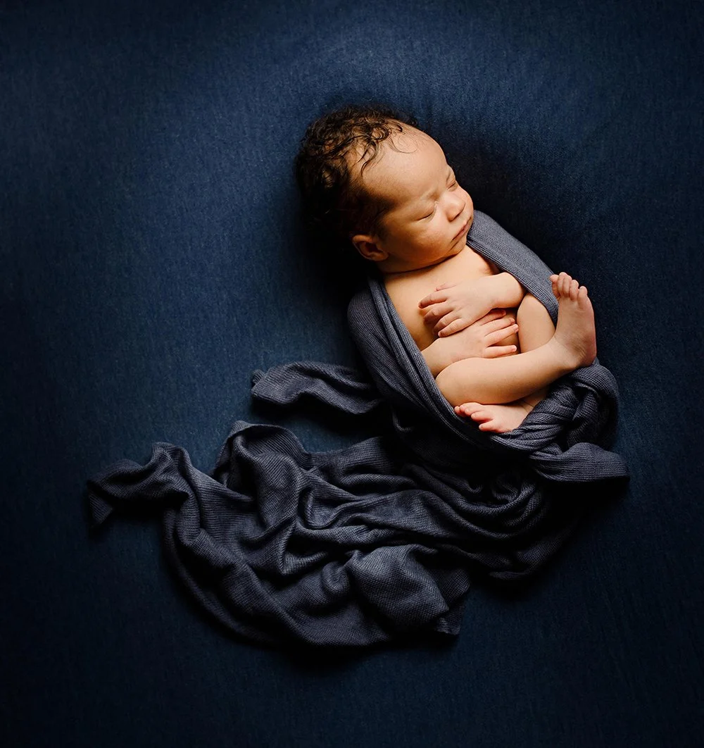 newborn baby wrapped in and sleeping peacefully on a navy blue blanket