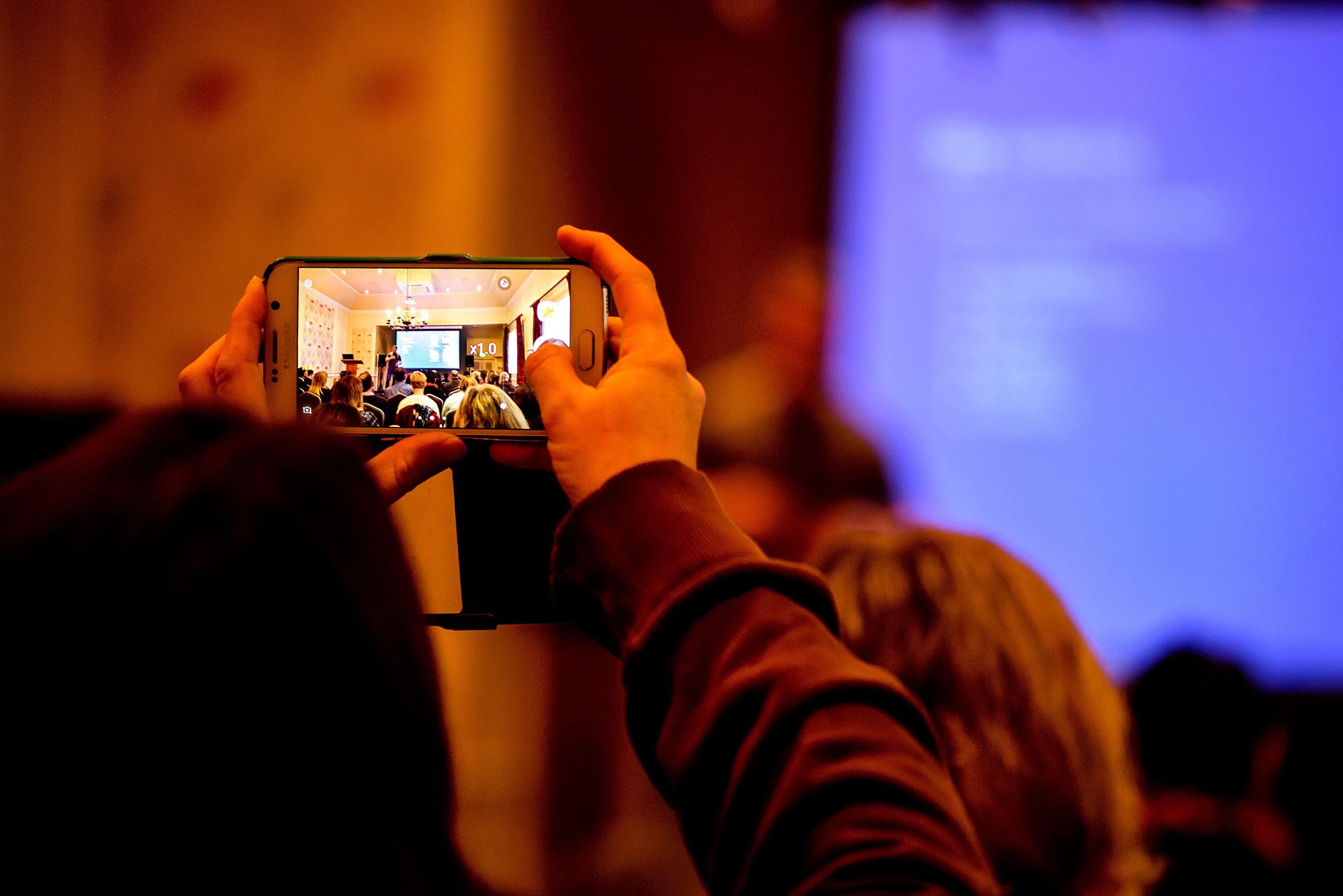 hands hold a mobile phone up hight to record a moment in a conference event