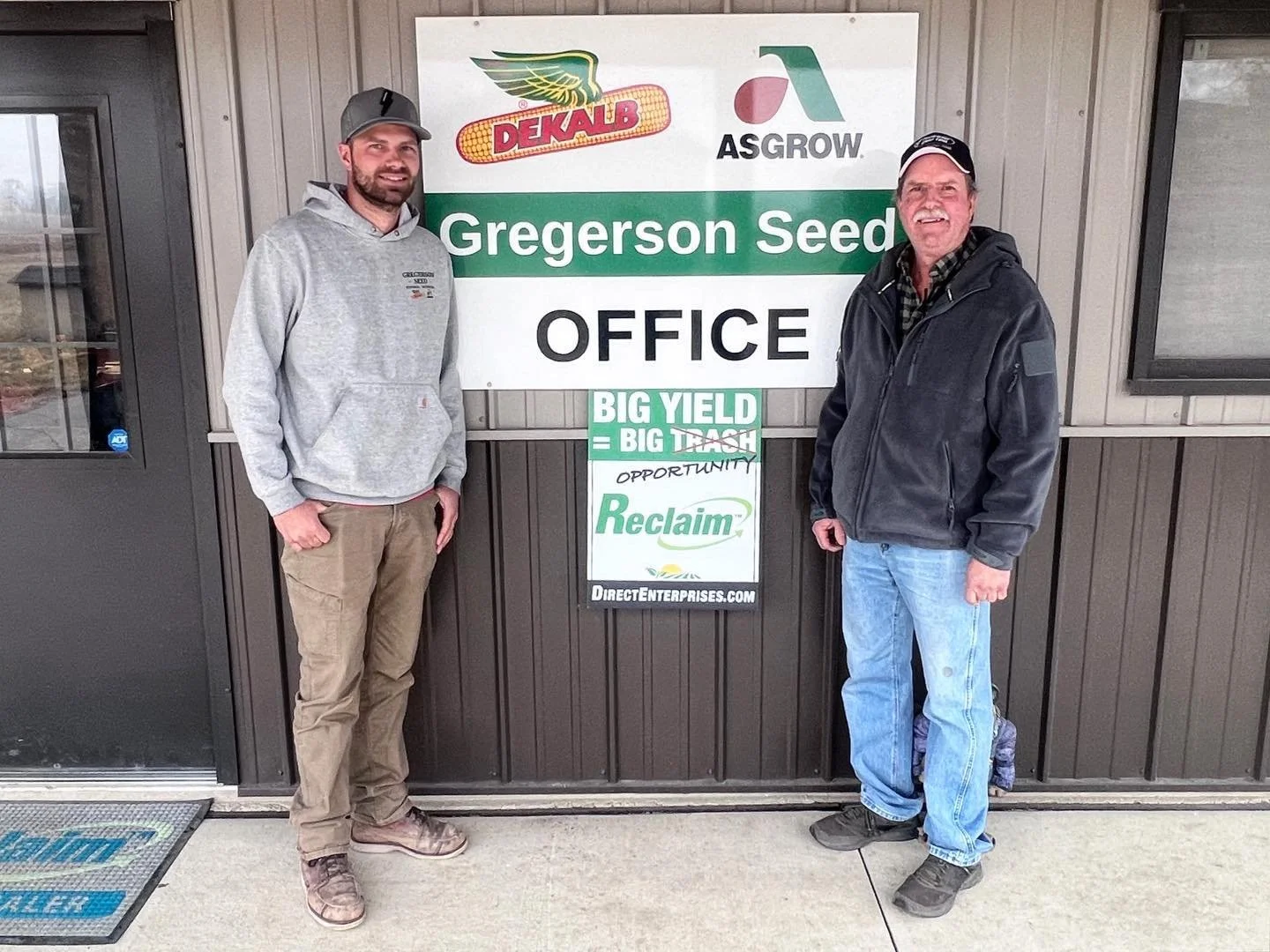 Three people standing in front of an agricultural exhibit booth with a green banner promoting starter fertilizer response on seed. The booth displays the logo "Fly By Acres LLC" and various farming images.