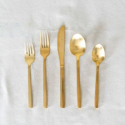 Gold-colored fork, knife, and three spoons arranged on a white cloth background.