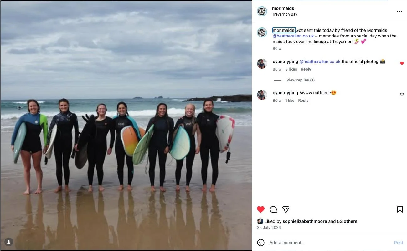 A group of female surfers posing for a photo on the beach holding their surfboards