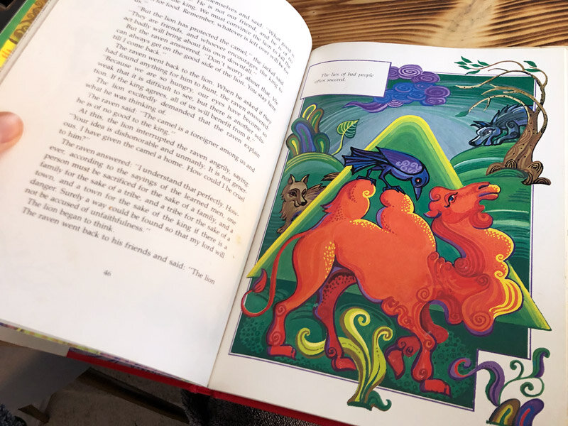 open book spread showing a colourful illustration of a raven standing on top of the hump of a camel by Anatole Ur