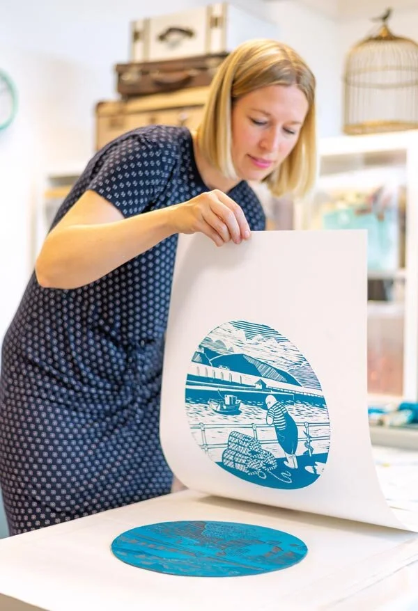 Heather Allen Skjervik holding a linocut print showing a fisherman at Portreath harbour