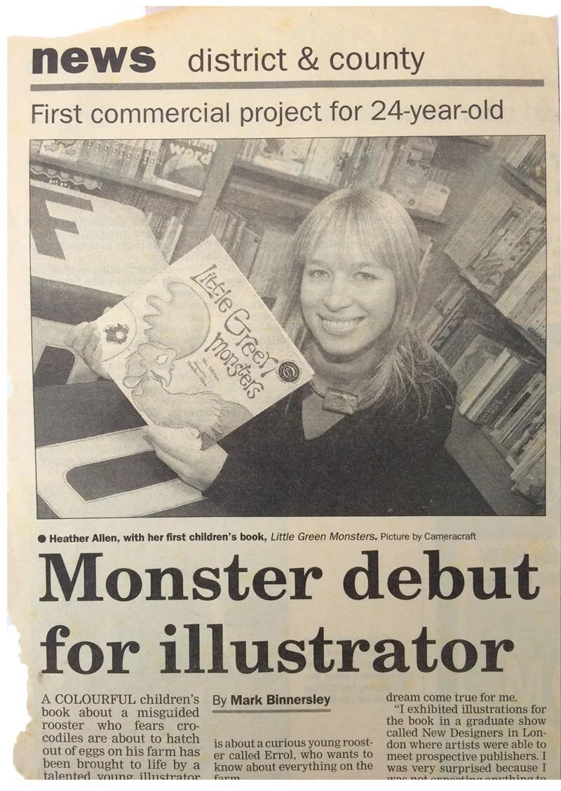 A young woman with blonde hair smiling at the camera, holding a children's book titled 'Little Green Monsters'. She is in a library with bookshelves in the background.