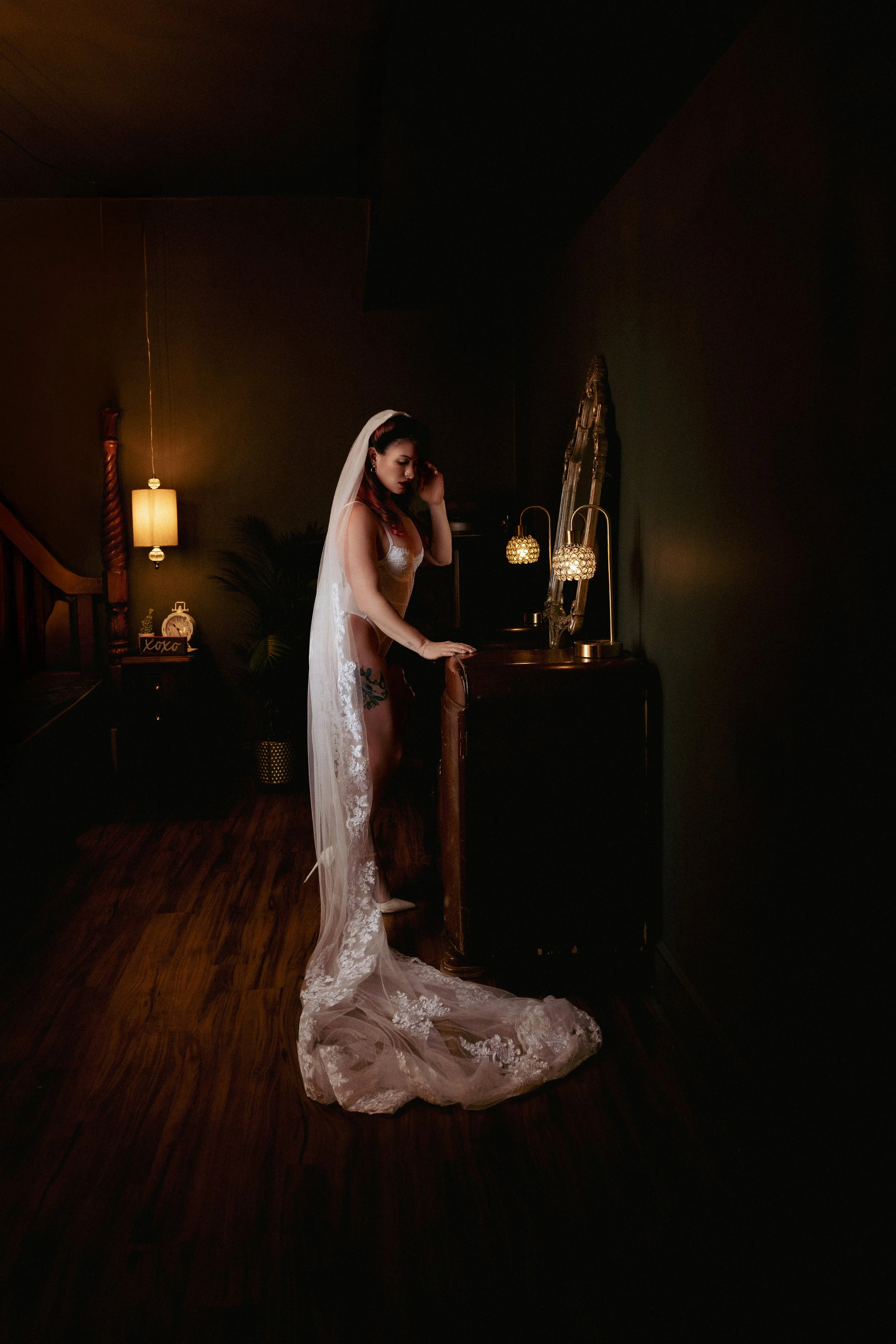 Elegant bridal boudoir image of a bride posing in front of a vintage vanity with her long veil pooled around her.