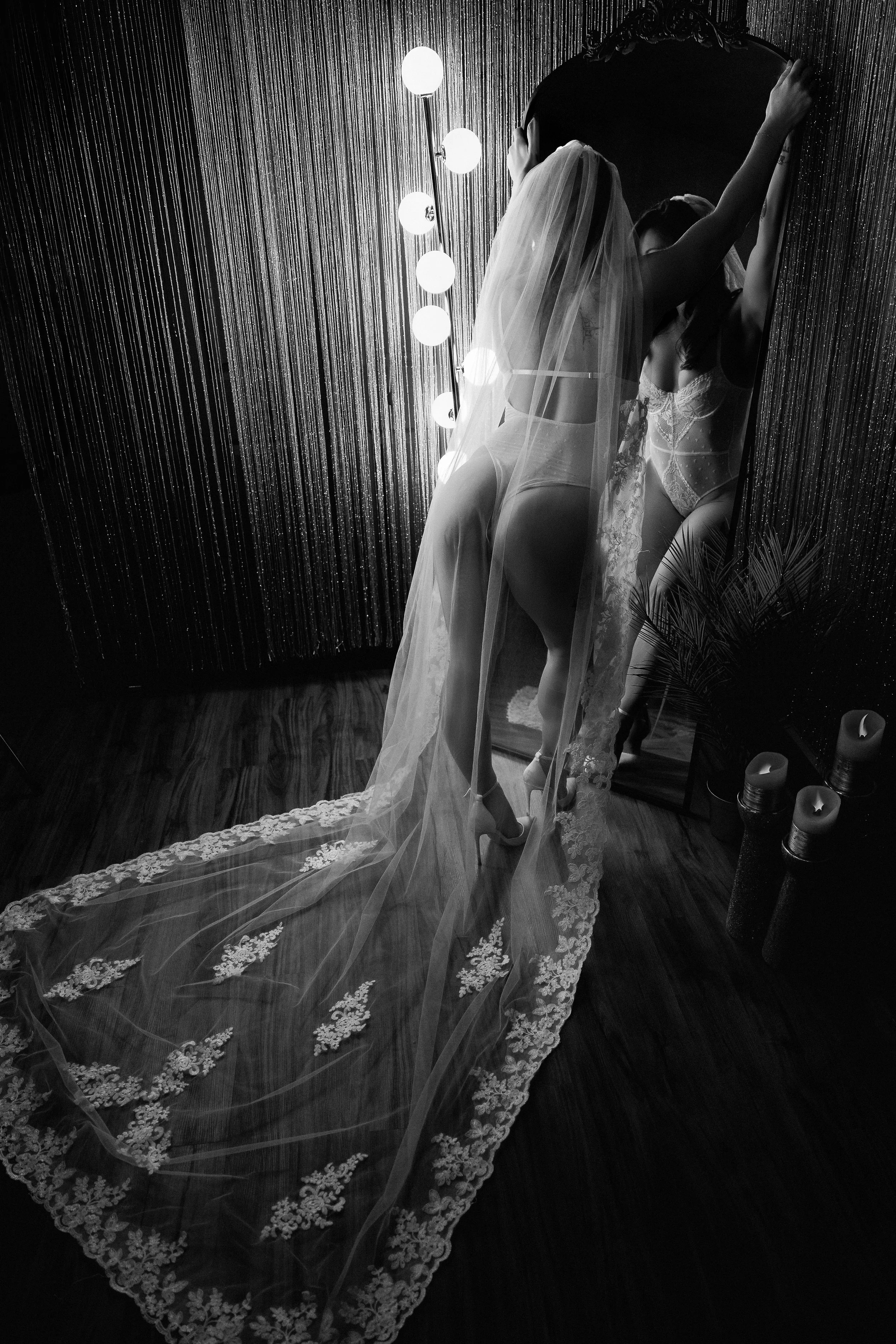 Luxury bridal boudoir scene with a bride in front of an antique vanity and an extended veil trailing on the floor.