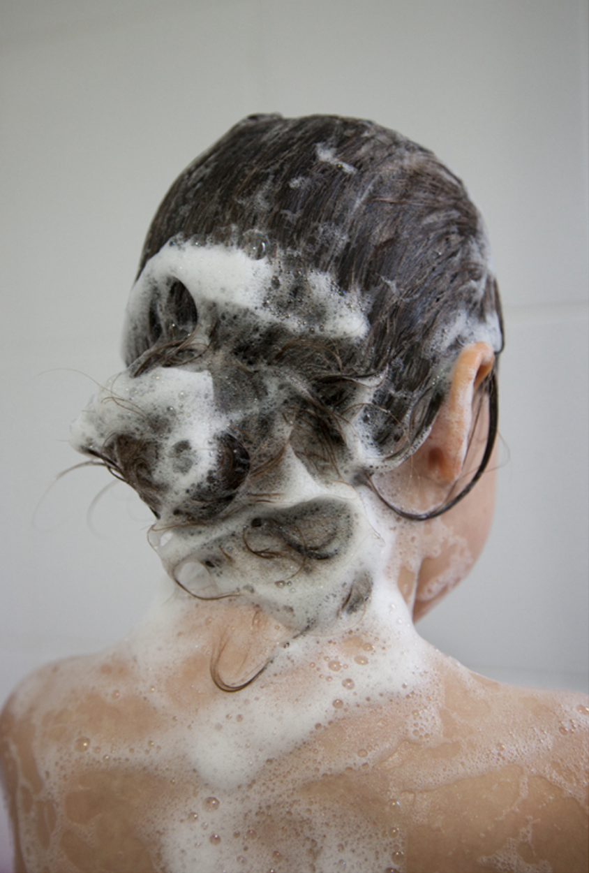 Person's head and shoulders covered in soapy lather during hair washing.