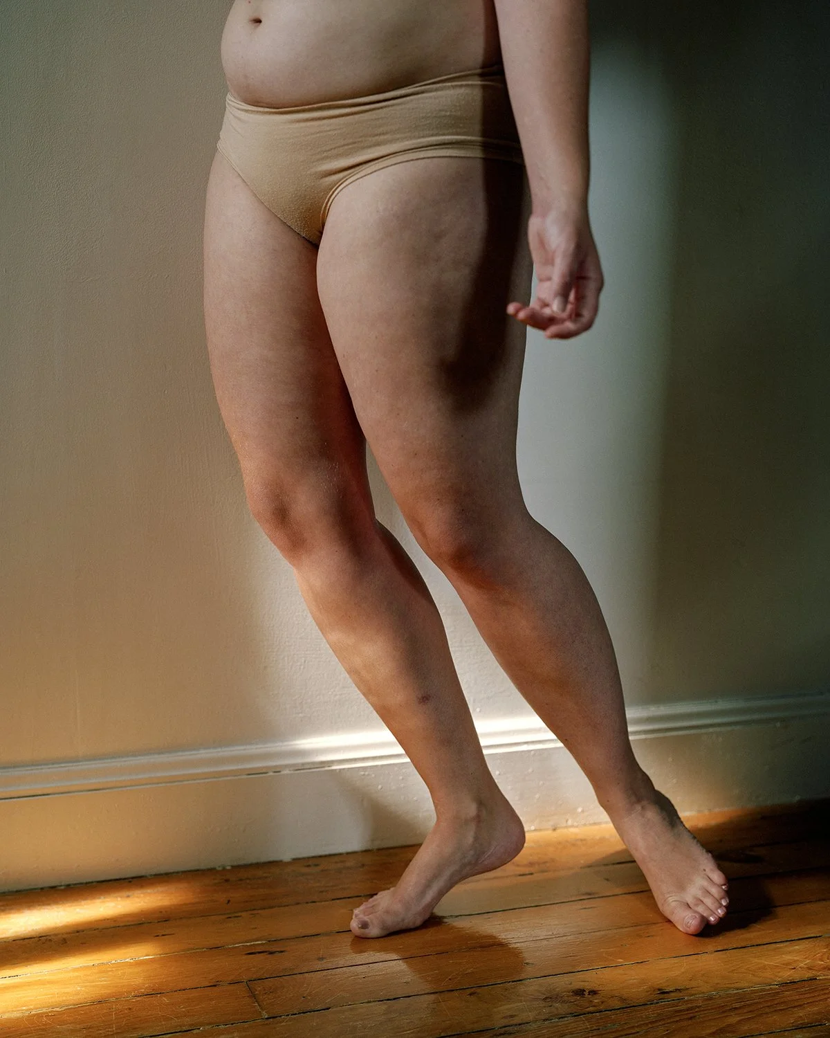 Person wearing beige underwear standing on a wooden floor with one leg slightly bent.