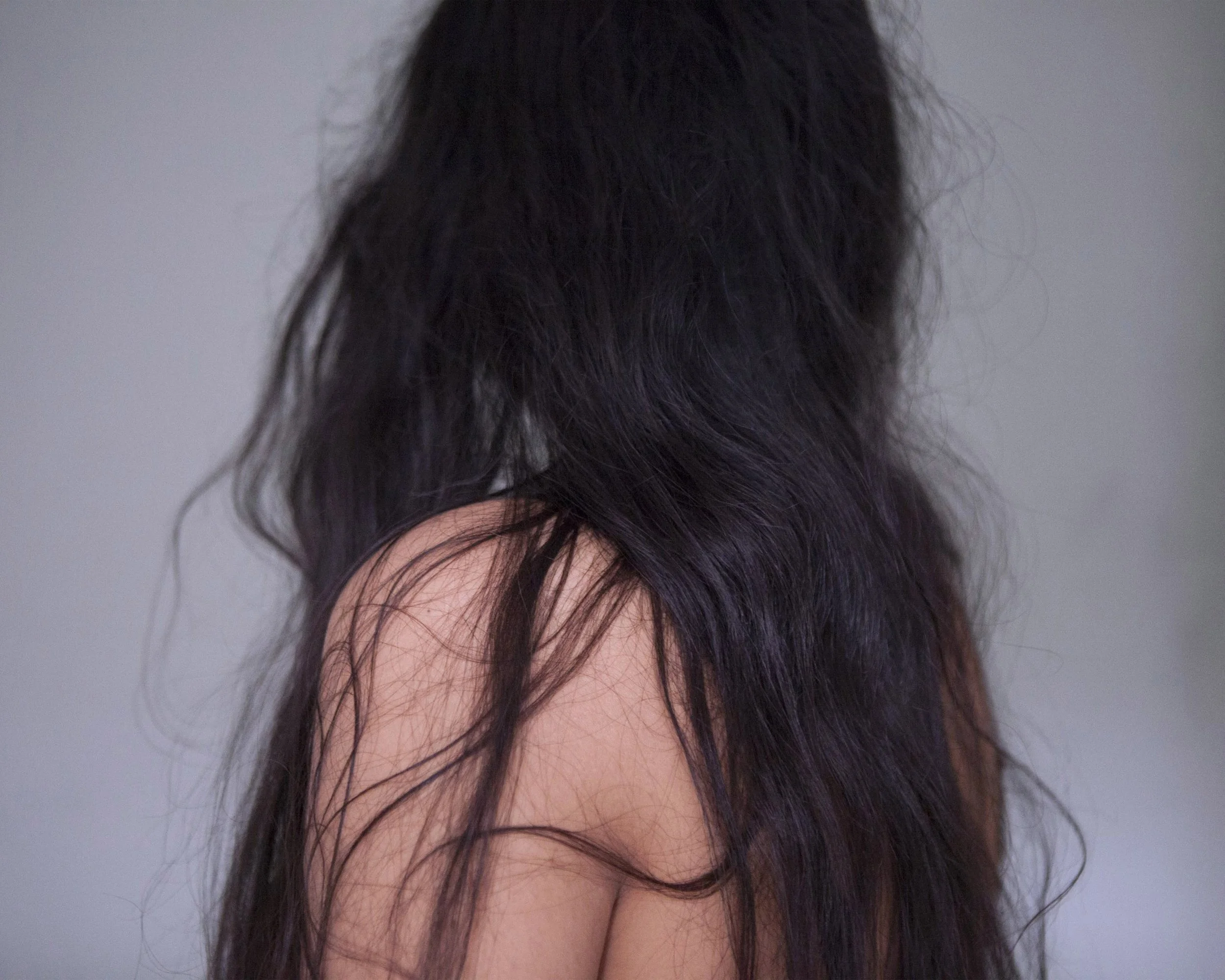 Person with long, dark, wavy hair from the back, bare shoulders visible.
