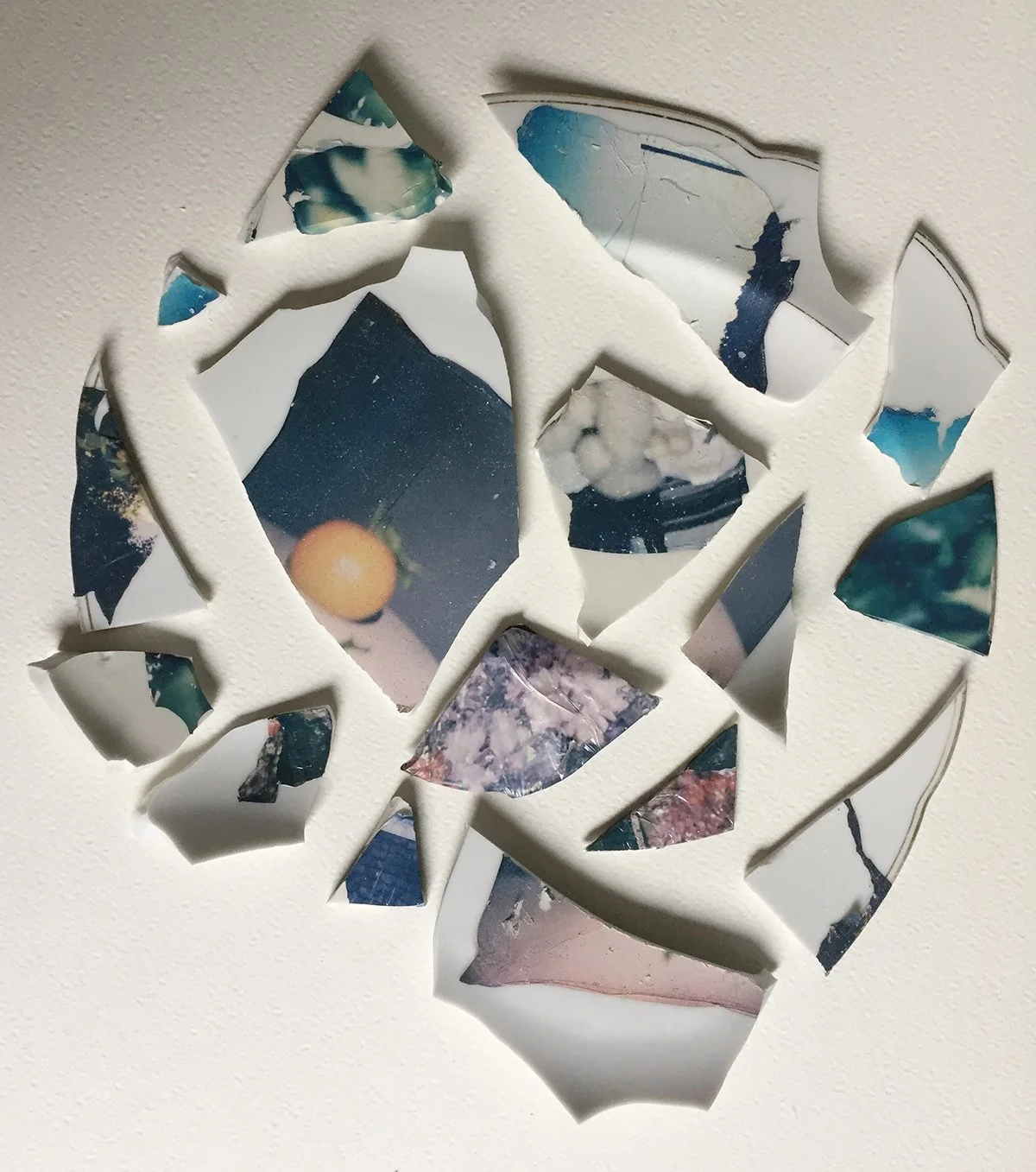 Broken pieces of a photograph on a white surface, showing various colors and partial images.