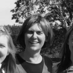 A woman smiling outdoors with trees in the background.