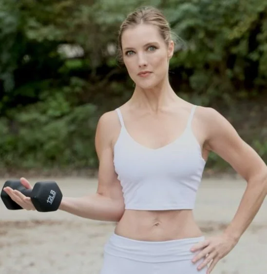Woman in white workout attire holding a 2 lb dumbbell outdoors.